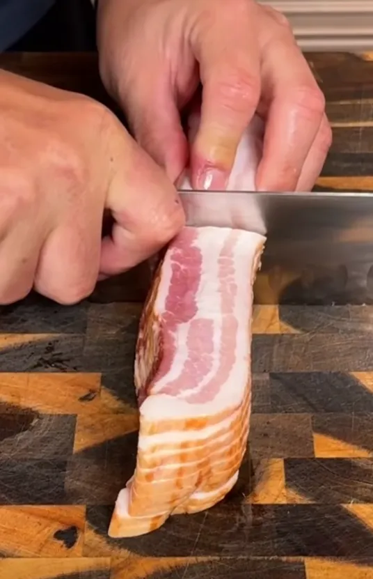 Streaky bacon being sliced in half on a wooden board