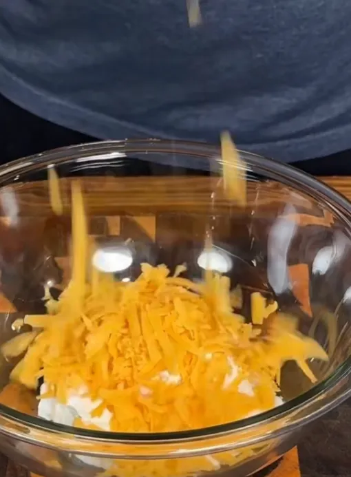 Grated cheddar cheese being added to the French onion dip in a bowl