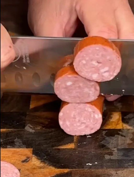 Smoked sausage being sliced into thick rounds on a wooden board