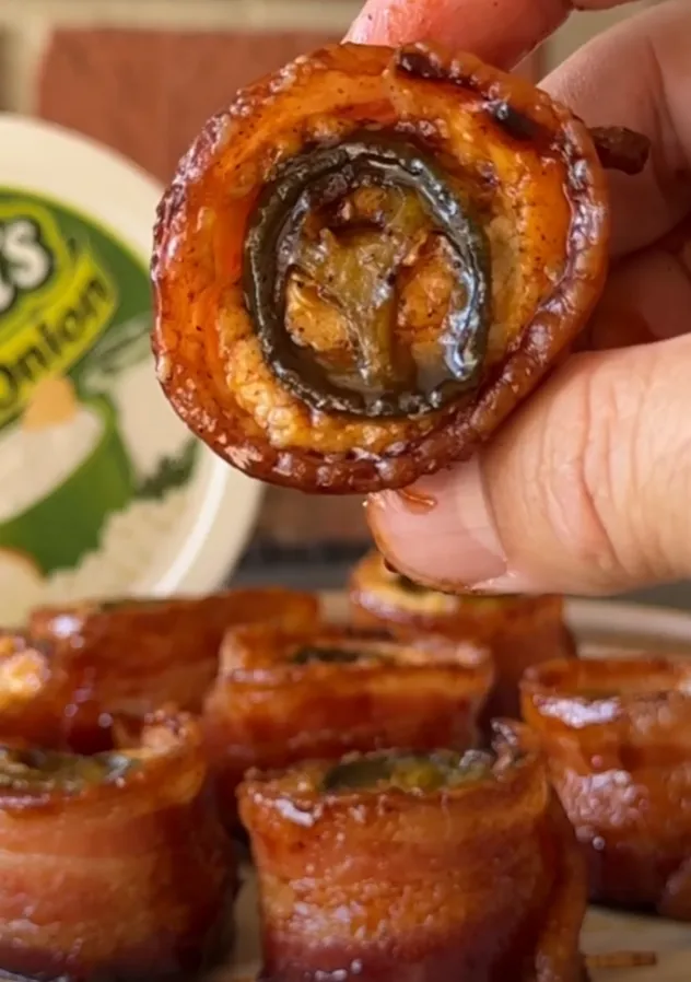 A finished bacon-wrapped sausage jalapeño popper held up, glazed and glossy