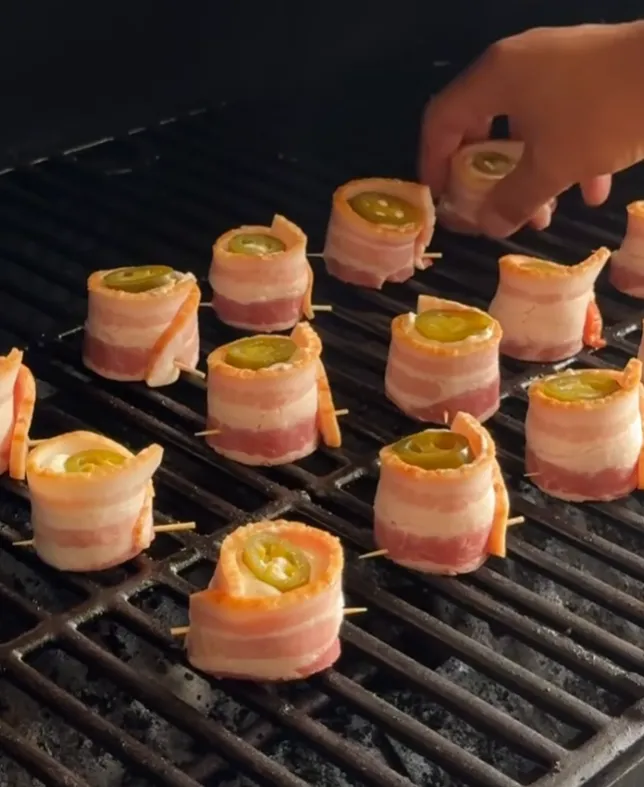 The bacon-wrapped poppers arranged on a smoker grill