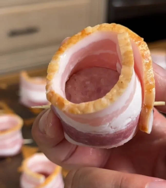 A sausage round wrapped in bacon and secured with a toothpick, forming a cup