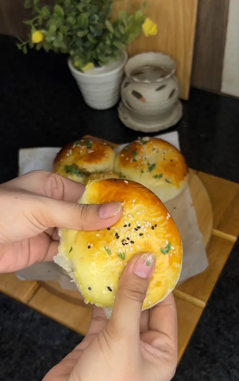 A hand holding a soft golden beef stuffed bun with a seeded top