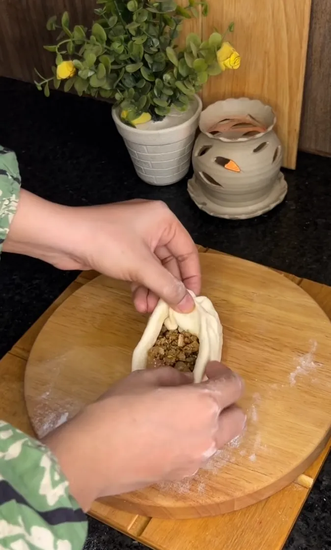 Dough being filled with spiced beef and sealed into a bun
