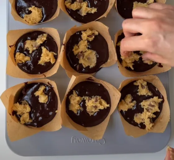 Muffin cups filled with brownie batter and topped with dollops of cookie dough, ready to bake