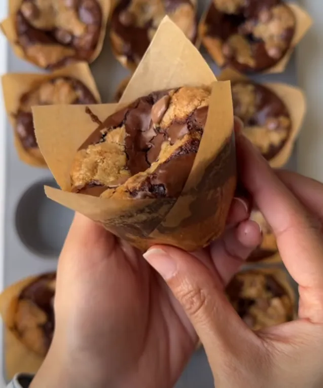 A brookie muffin in its tulip wrapper, held up to show the cookie-topped brownie
