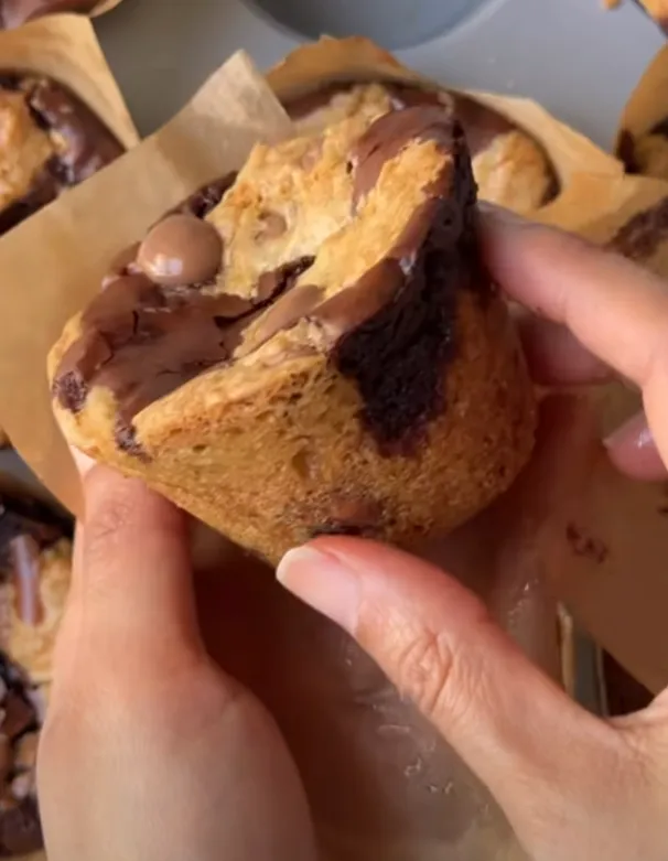 A brookie muffin torn open to show the gooey brownie and cookie inside