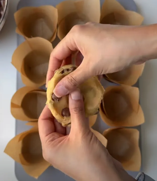 A ball of cookie dough pressed into the bottom of a tulip-lined muffin cup