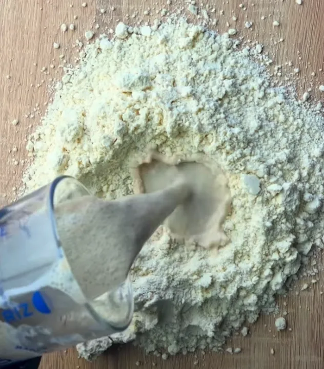 The foamy yeast liquid being poured into a well in the flour