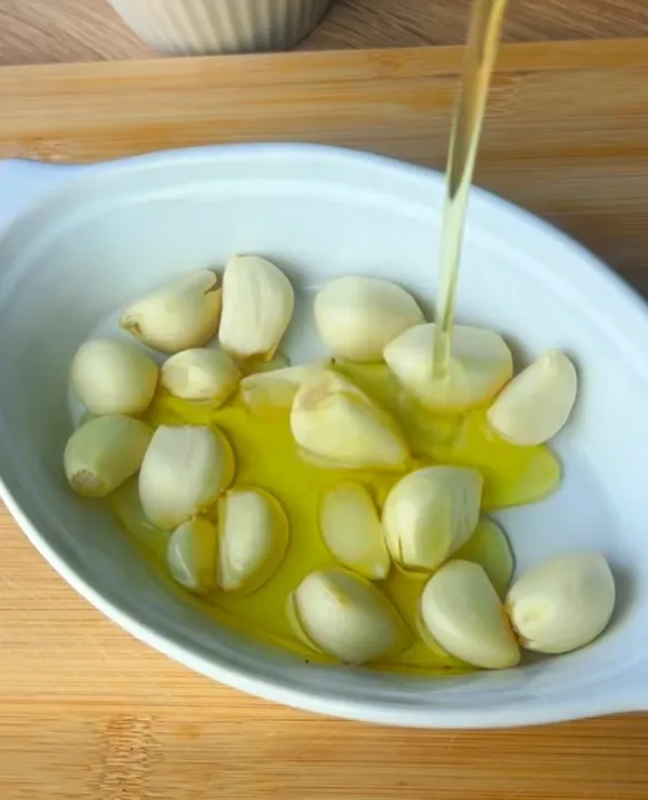 Olive oil being poured over the garlic cloves before roasting