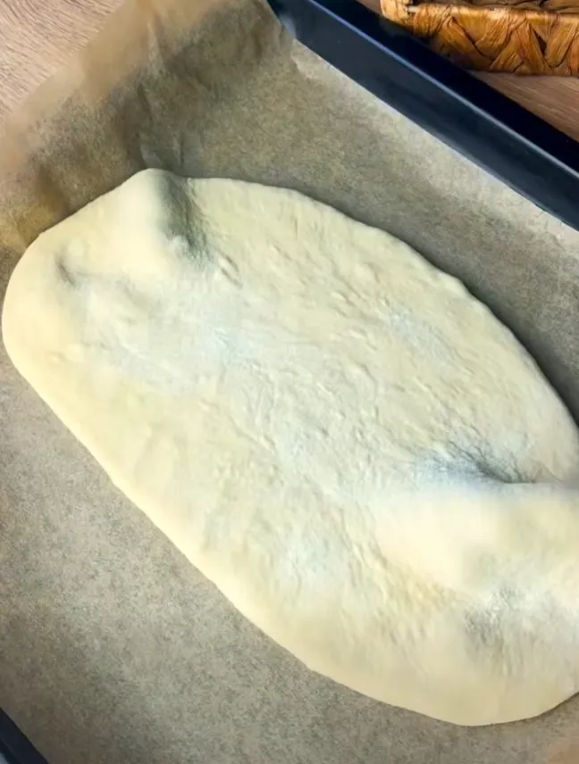 Risen dough stretched into an oval on a lined baking tray