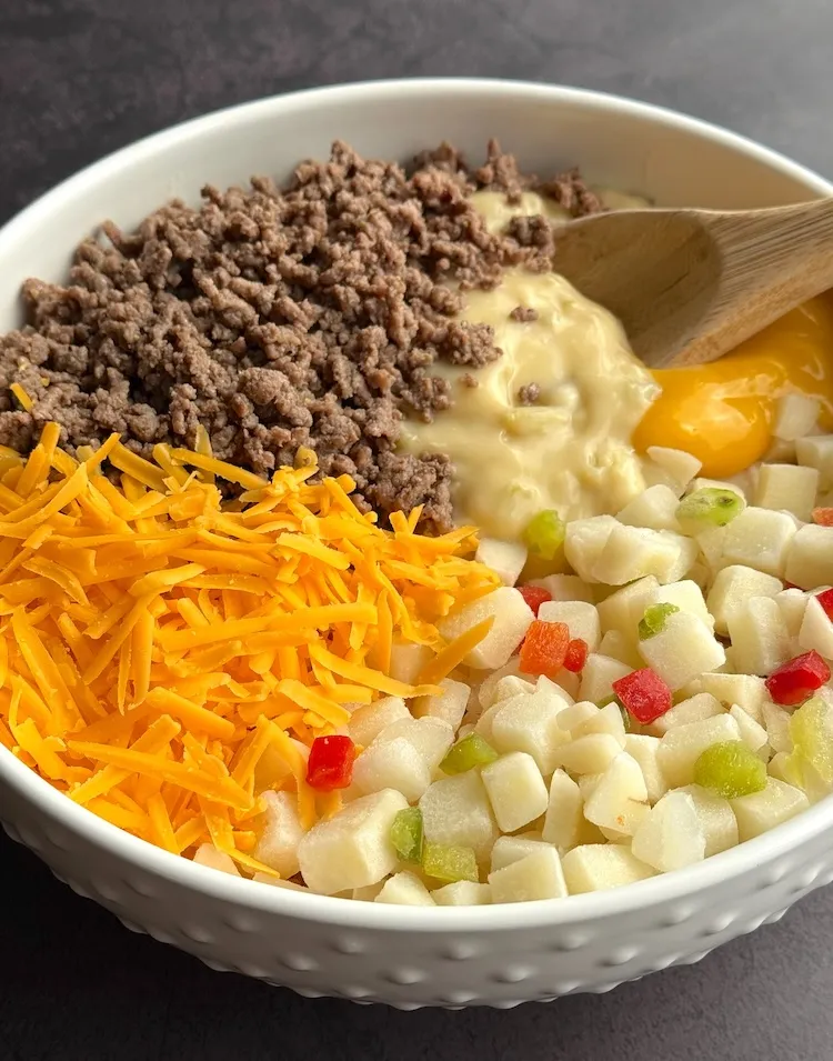 Frozen potatoes, ground beef, two soups and shredded cheddar in a bowl before mixing