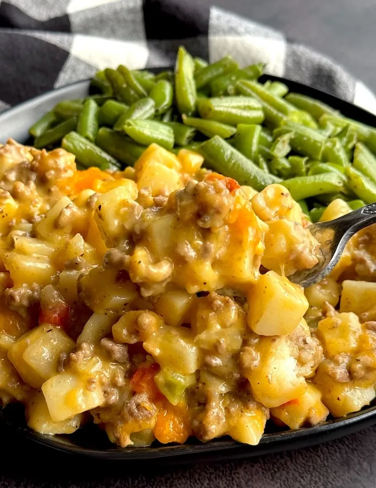 Cheesy ground beef and potato casserole served on a plate with green beans