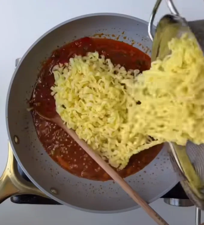 Cooked ramen noodles being added to the chili garlic sauce