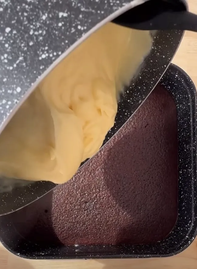 Pale milk cream being poured over the baked chocolate sponge