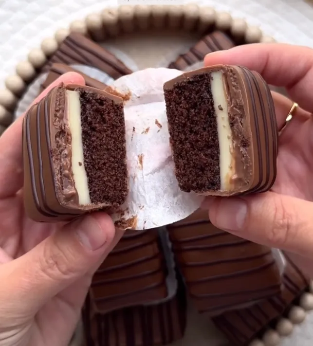 Two halves of a snack cake bar held up to show the chocolate sponge, milk cream and chocolate coating