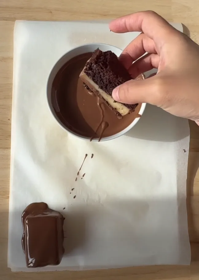 A snack cake bar being dipped into a bowl of melted chocolate