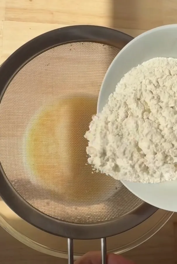 Flour being sifted into the wet chocolate cake mixture