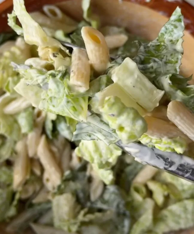 A close-up of crispy chicken caesar pasta salad showing penne, romaine and creamy dressing on a fork