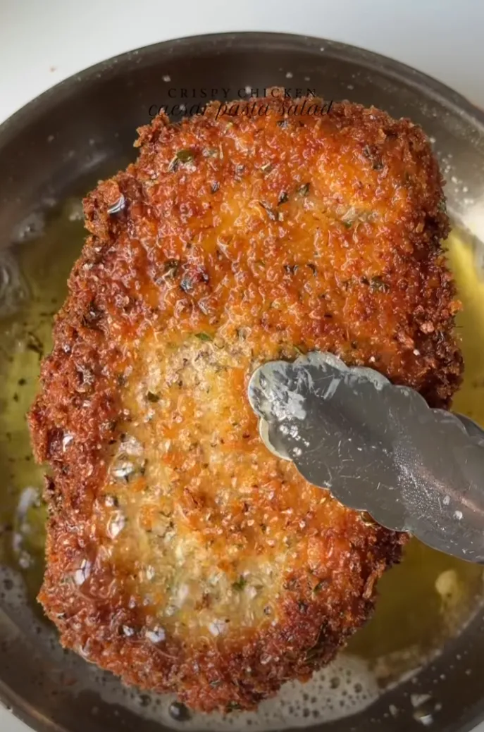 A golden, panko-crusted crispy chicken breast frying in oil