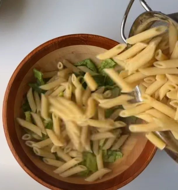 Chopped romaine lettuce and penne pasta in a wooden salad bowl