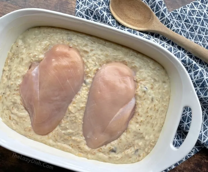 Creamy rice mixture spread in a baking dish with two raw chicken breasts on top