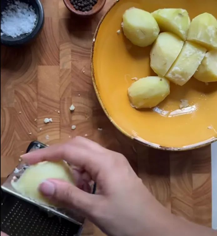 Par-boiled potatoes being coarsely grated on a box grater