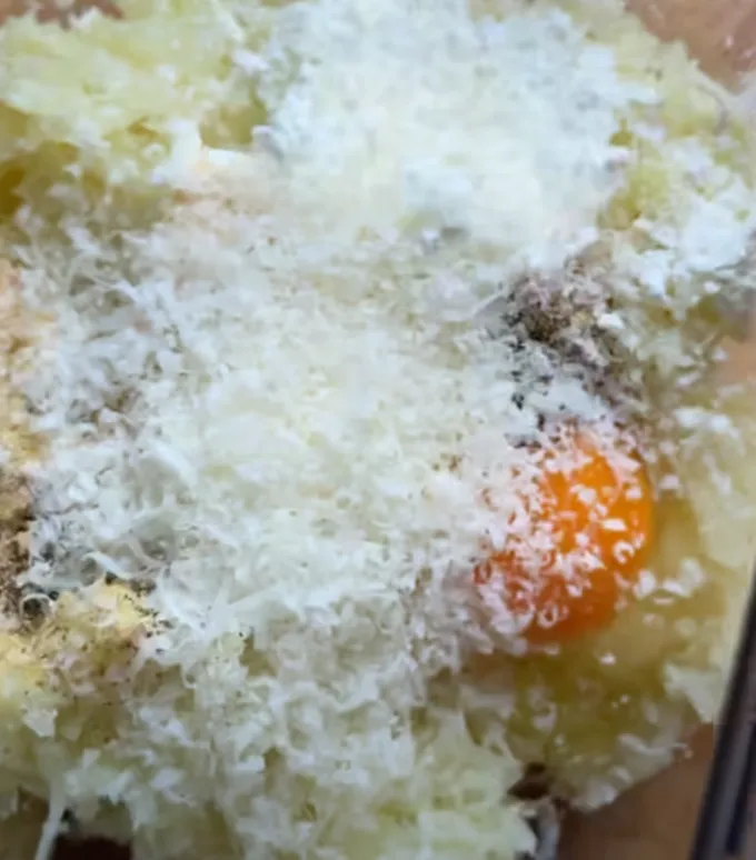 Finely grated parmesan being added to the seasoned grated potato