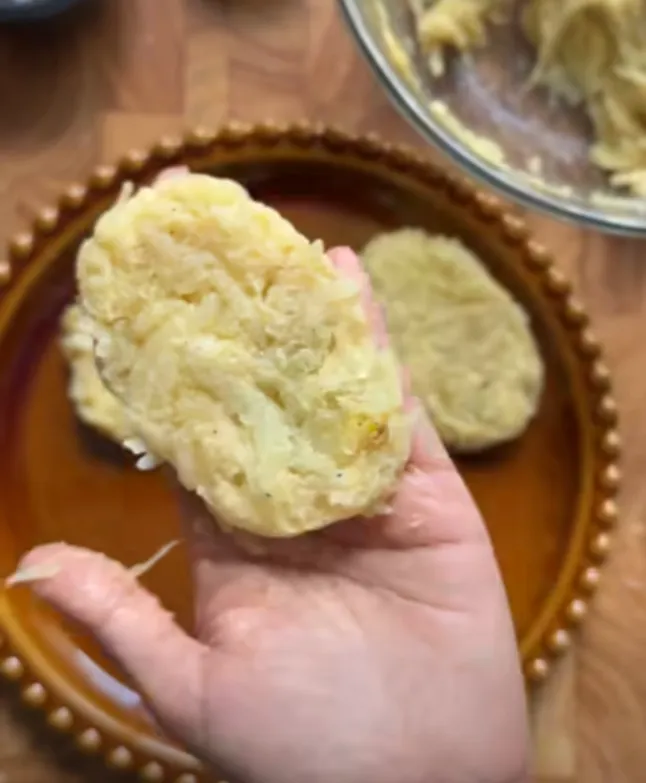 A shaped garlic parmesan hashbrown patty held in hand before frying