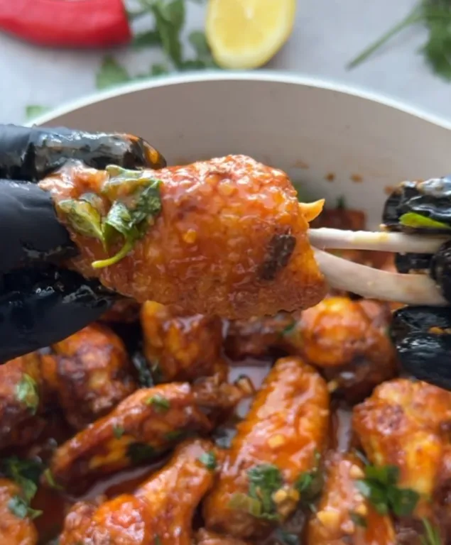 A close-up of a sticky honey chilli lemon chicken wing held up over the pan