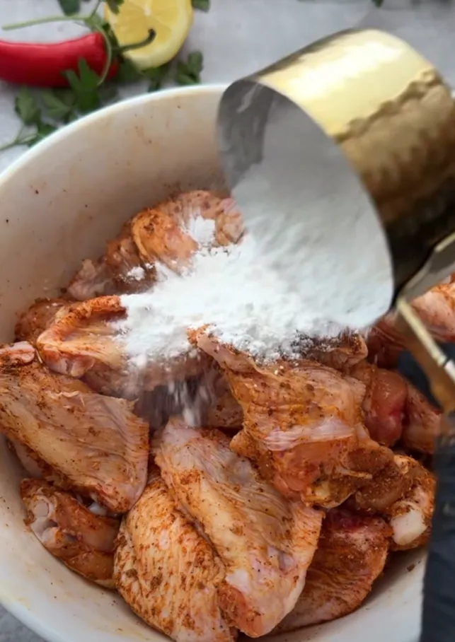 Cornflour being sprinkled over the seasoned chicken wings in a bowl