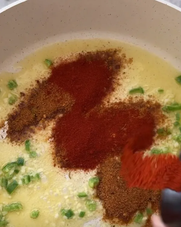 Paprika and chilli spices being added to the buttery sauce base in the pan