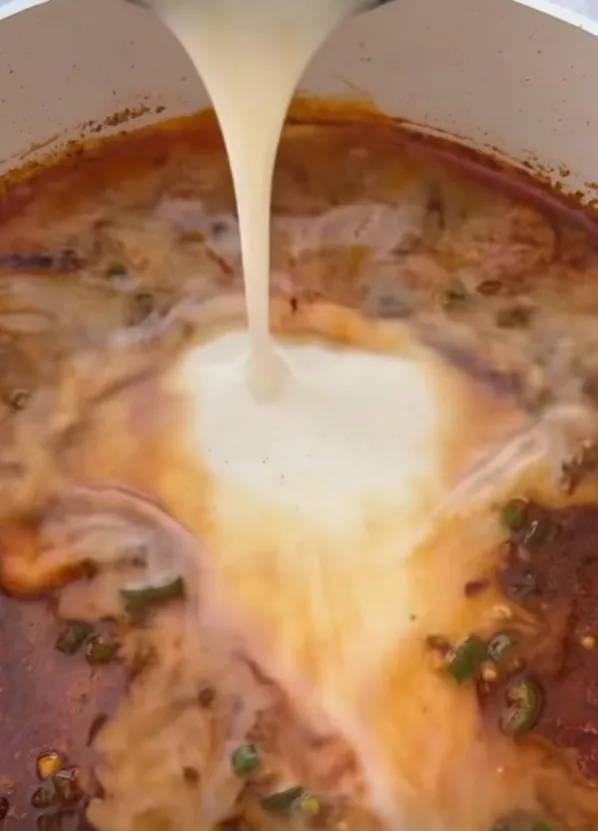 A pale cornflour slurry being poured into the dark glossy sauce to thicken it