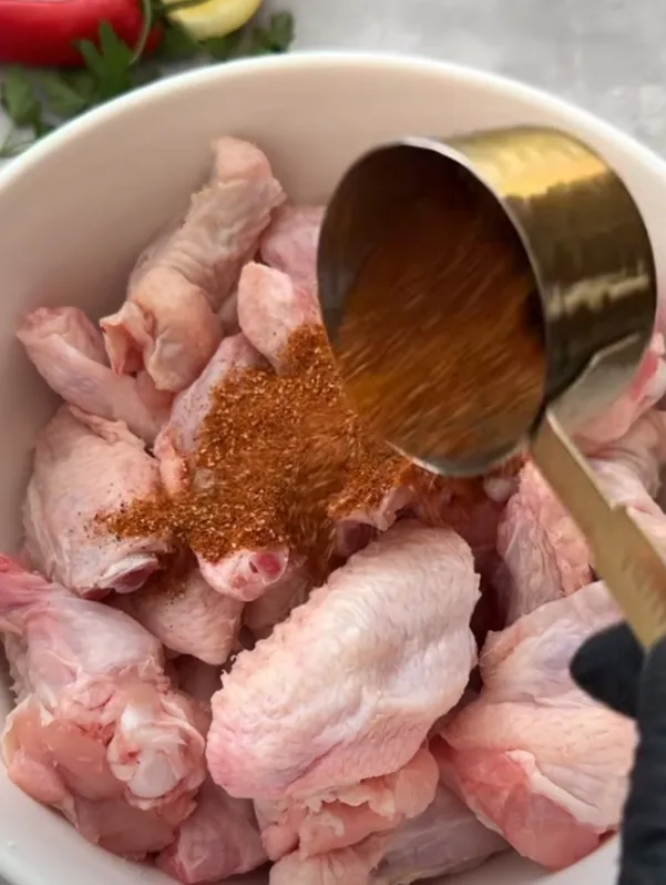 Raw chicken wings in a bowl with spice rub being poured over them