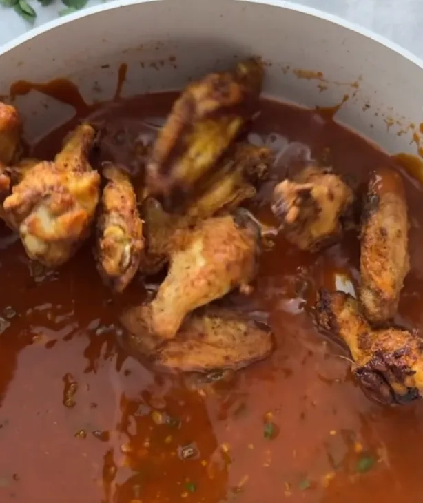 Crispy air-fried chicken wings being added to the sticky sauce in the pan