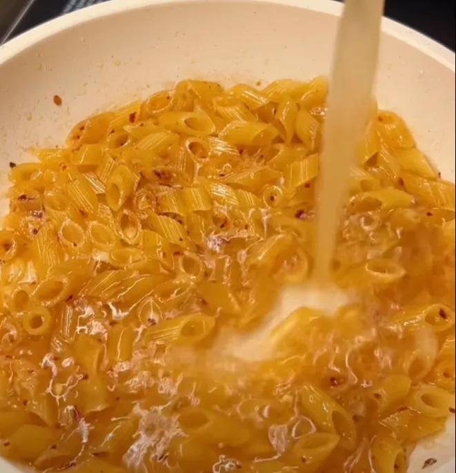 Water being poured over the toasted penne to cook it in the pan