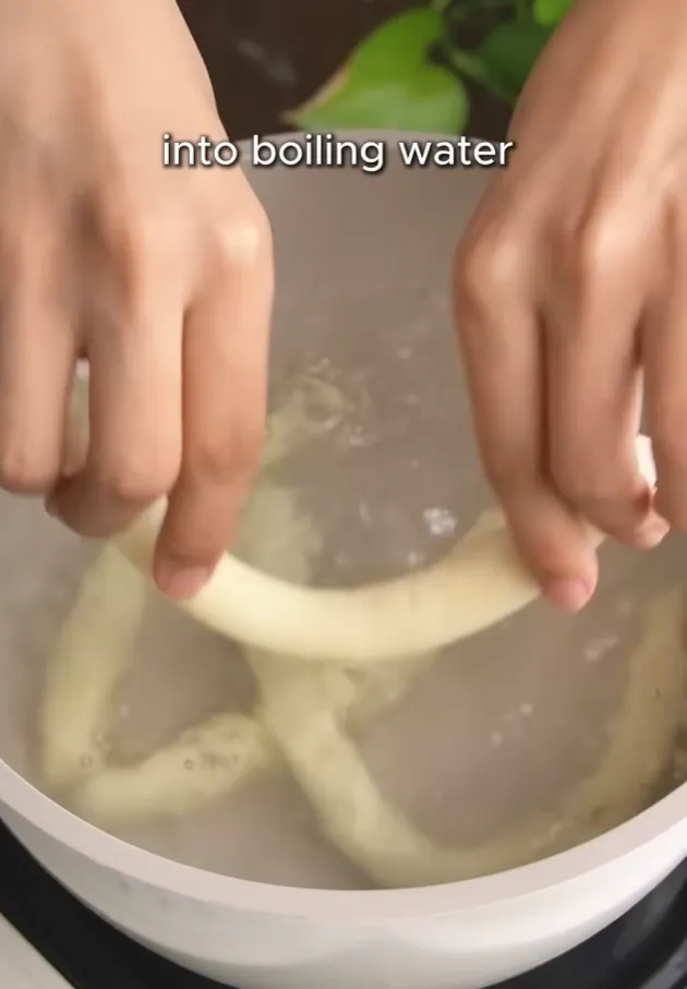 Potato noodle ropes being lowered into a pot of boiling water