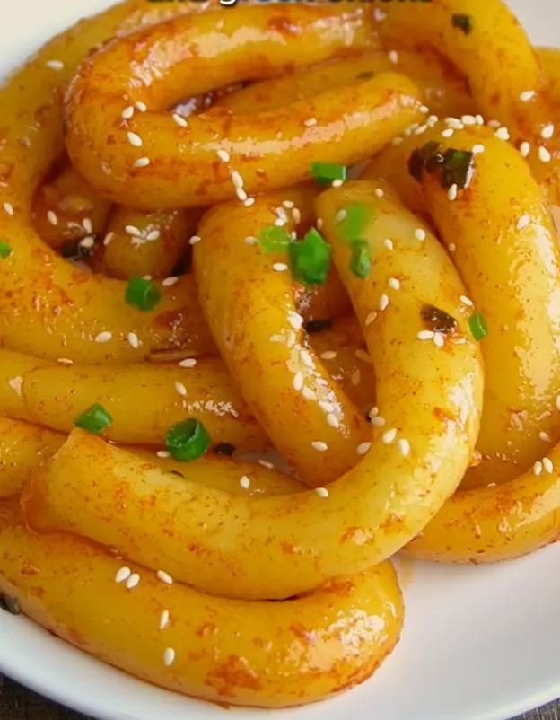 A close-up of glossy spicy potato noodles coated in red chili oil and sesame seeds