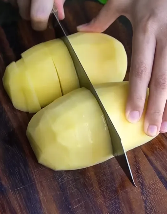 Peeled potato being cut into chunks on a wooden board