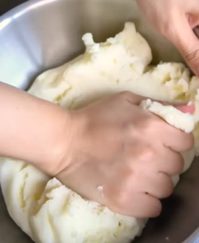 Hands kneading the smooth potato dough in a metal bowl