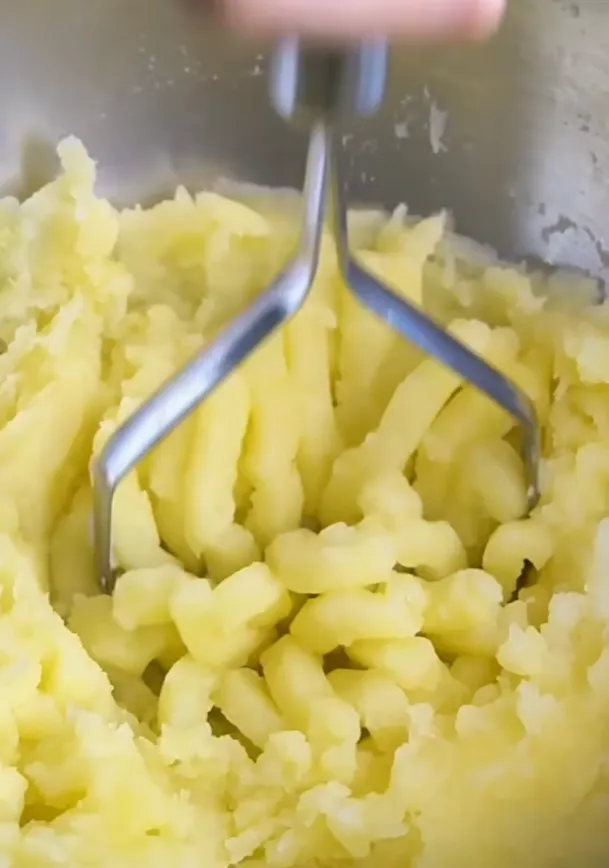 Boiled potato being mashed smooth with a masher