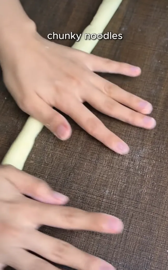 A thick potato noodle rope being rolled out by hand on a dusted surface