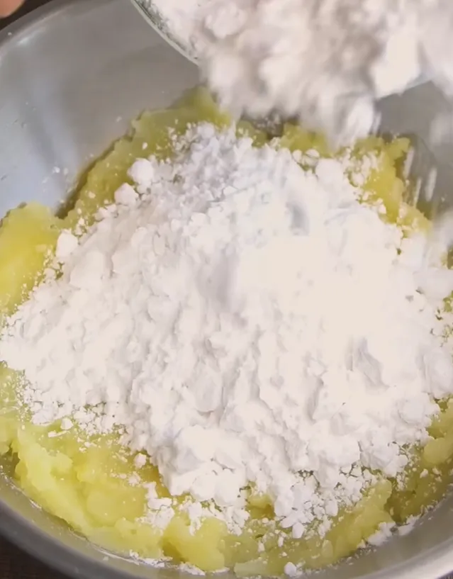 Potato starch being added to warm mashed potato in a bowl