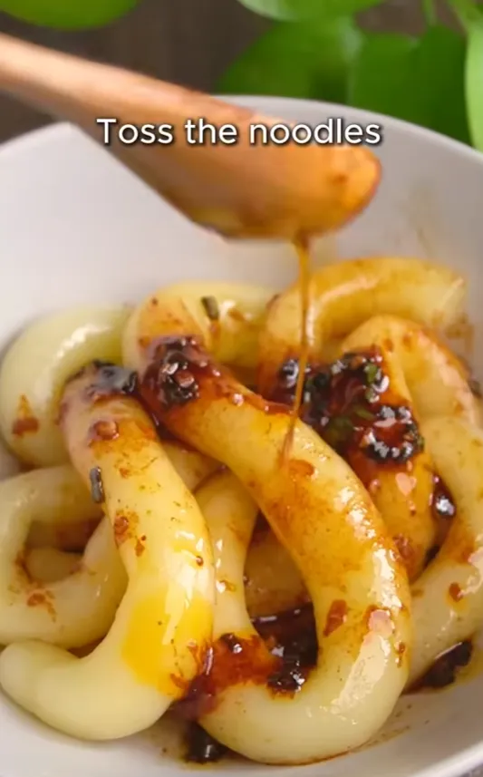 Spicy red chili sauce being tossed through the chewy potato noodles